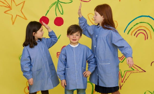 Trois enfants en blouses bleues qui lèvent la main